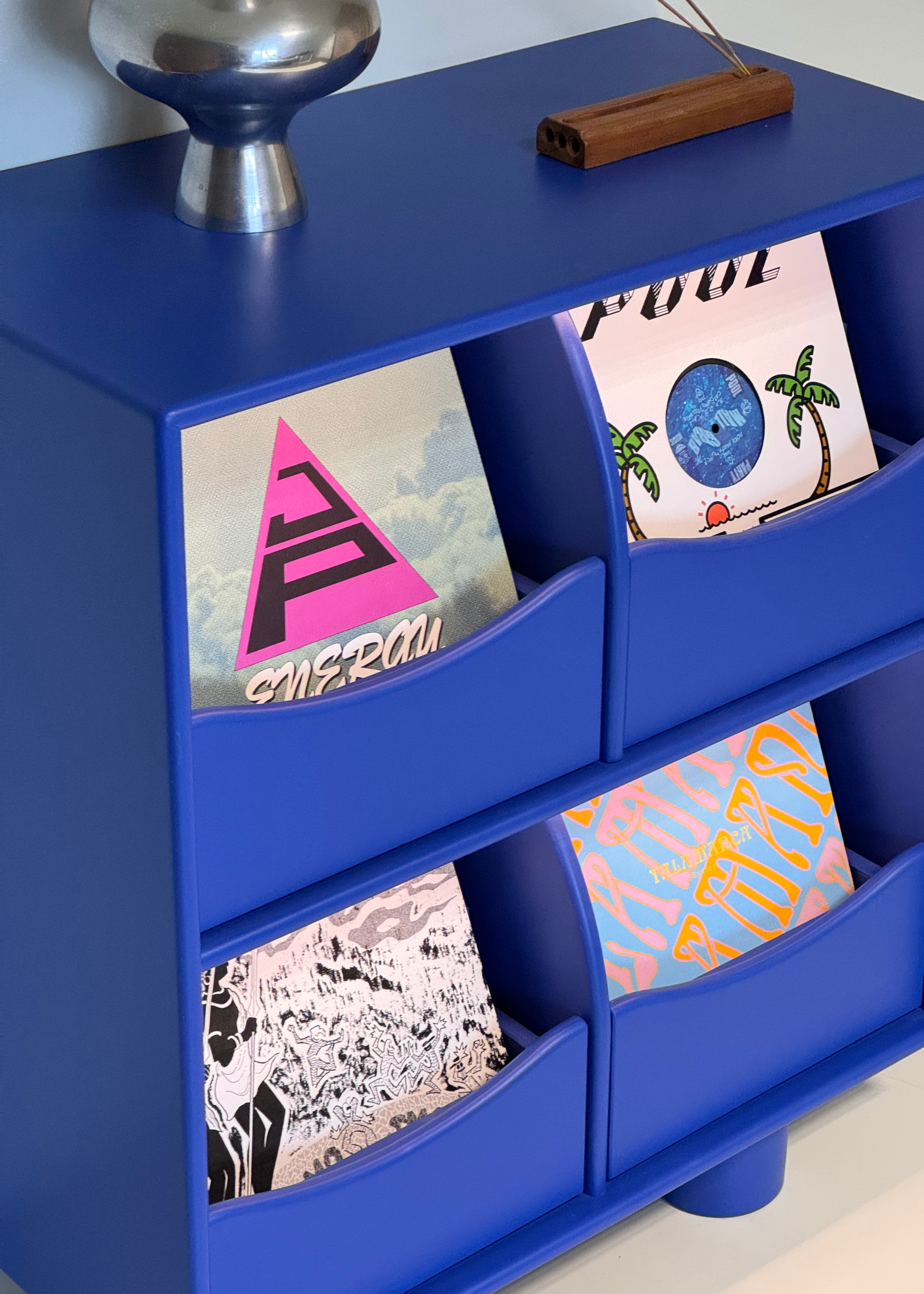 A cobalt blue record bar with a collection of vinyl, an incense holder and a chrome vase