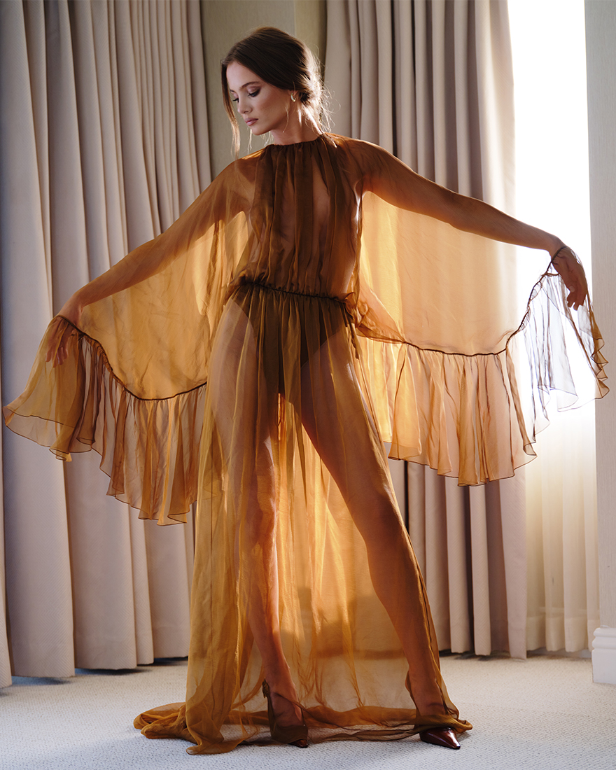 Freya Allan poses with arms out wearing sheer bronze YSL dress.