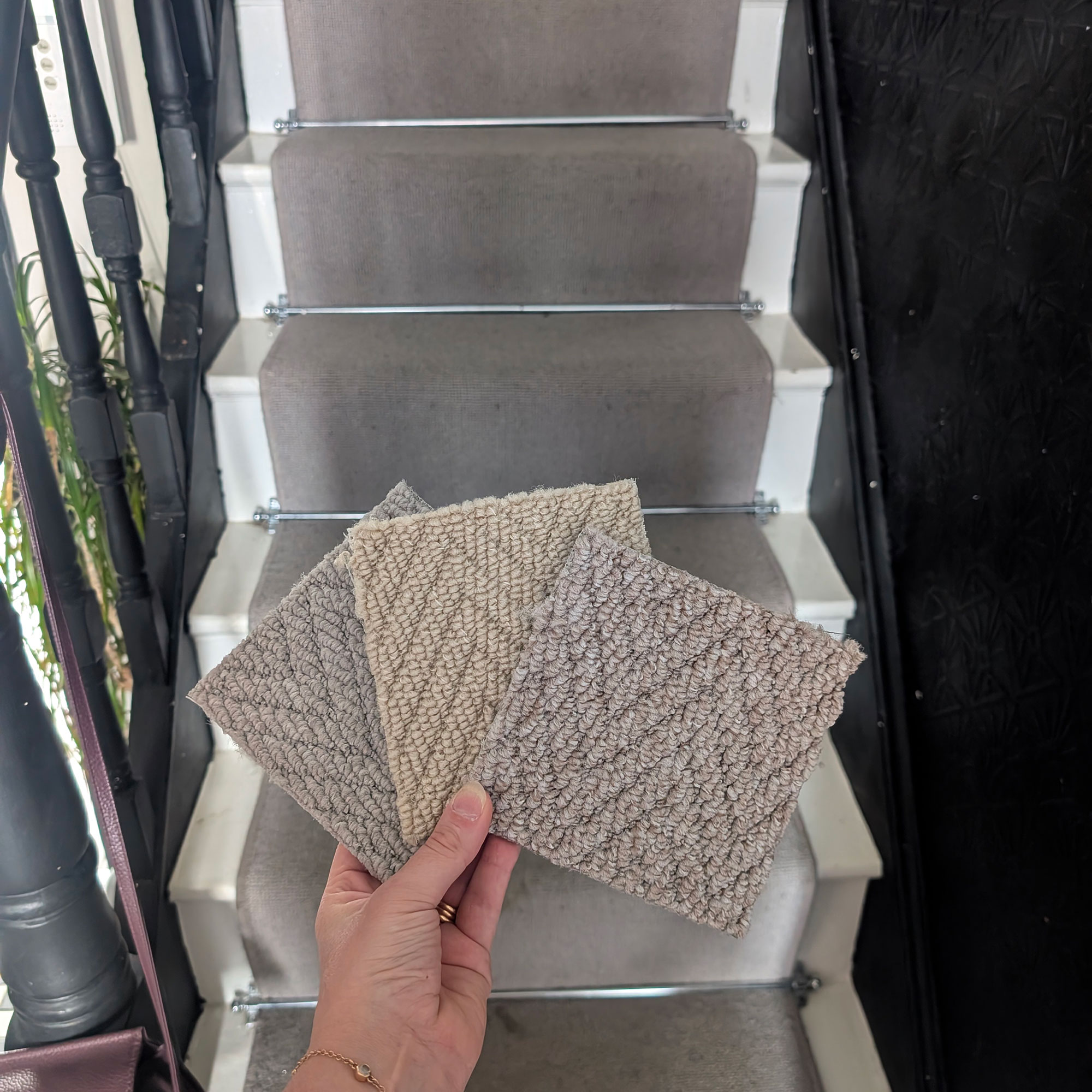Person holding three carpet samples in front of grey-carpeted staircase