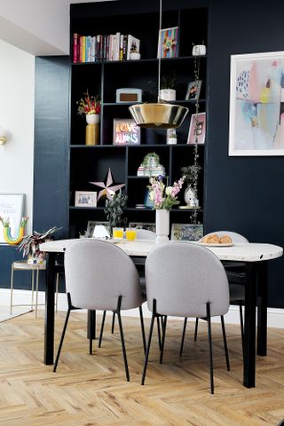 Dining area with terrazzo-topped table, grey chairs, herringbone wood floor, metallic pendant light and blue open shelving filled with accessories