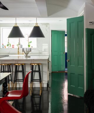 accents colors for a white kitchen, monochromatic kitchen with emerald green accent doors, black floor, black and brass pendants and bar stools, red chair