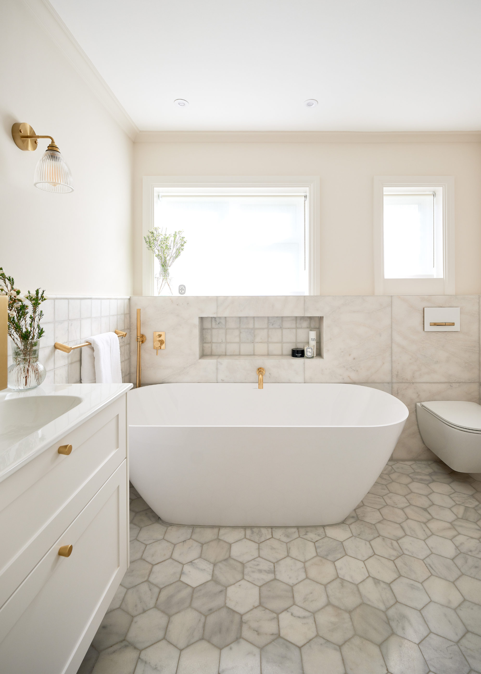 a light, airy bathroom with honeycomb marble tiled floors, a large white free standing tub and gold hardware