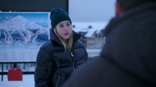 Hanna wearing a woolly hat with a puffer coat looking at someone off-camera in The Åre Murders.