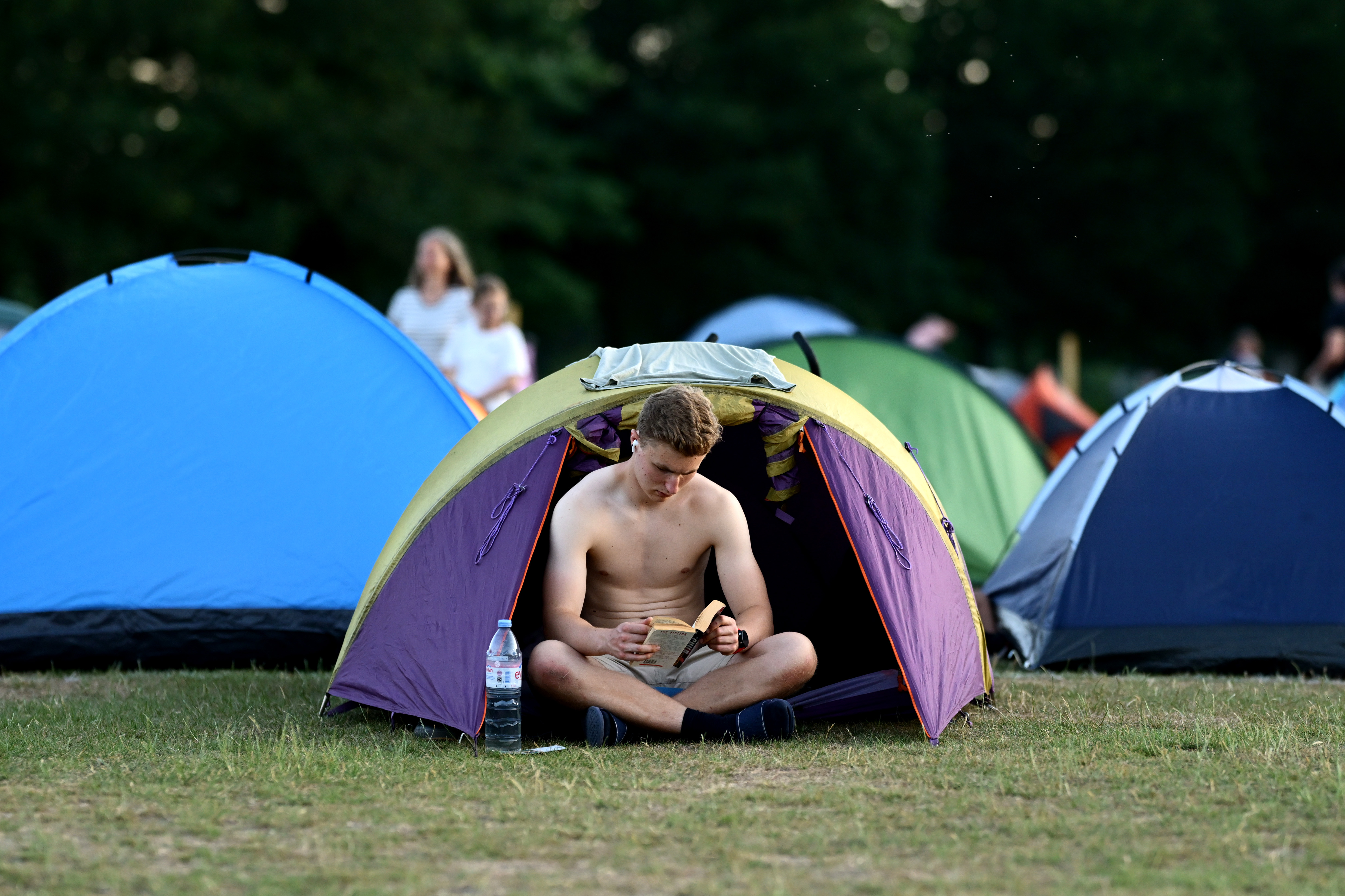 A spectator reads outside his tent in Wimbledon Park the night before the start of The Championships Wimbledon 2025 at All England Lawn Tennis and Croquet Club