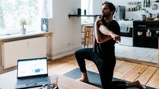 Man stretches on a yoga mat as he takes a break from his laptop screen