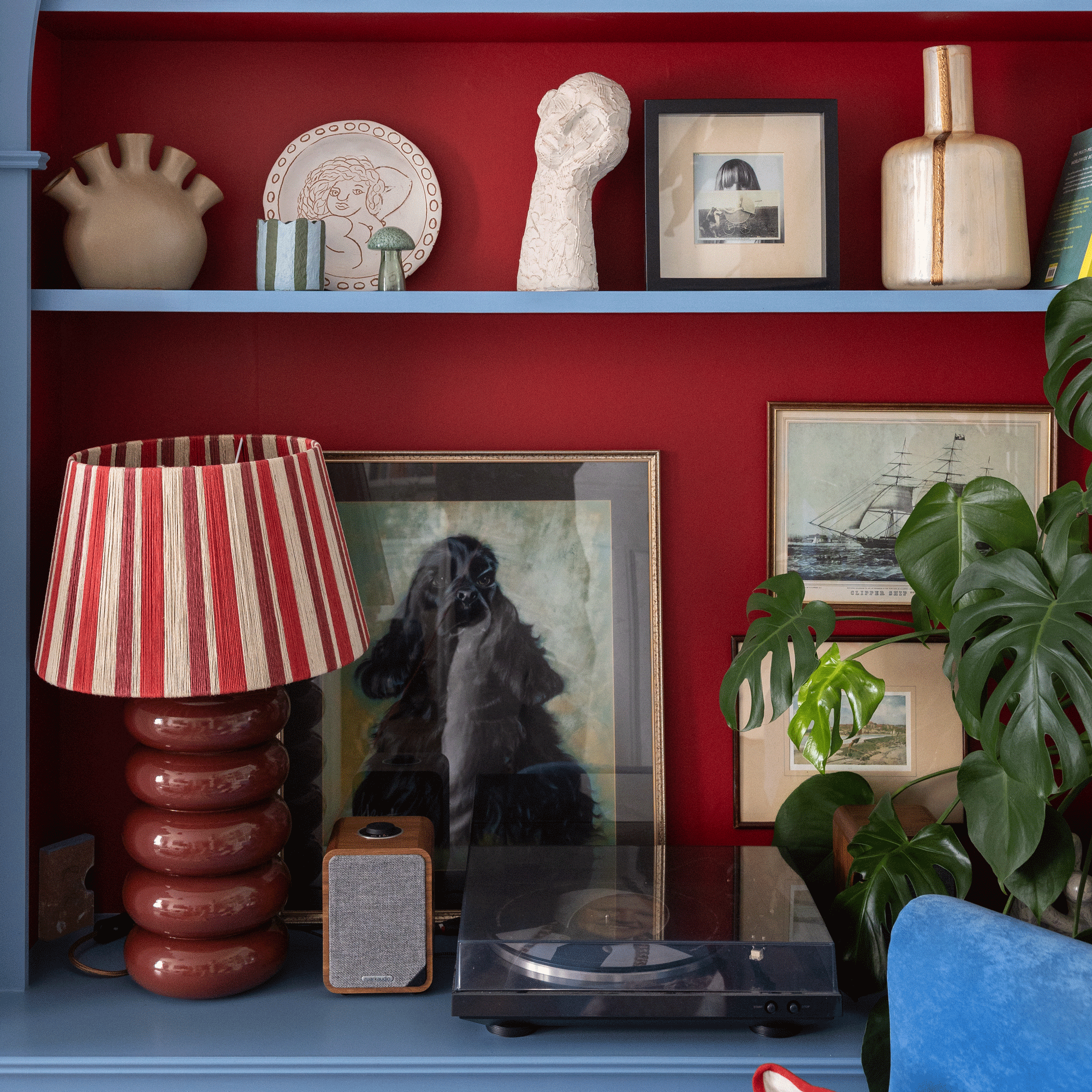 detail image of alcove shelving painted in bright blue and dark red, with art, a record player and table lamp and accessories
