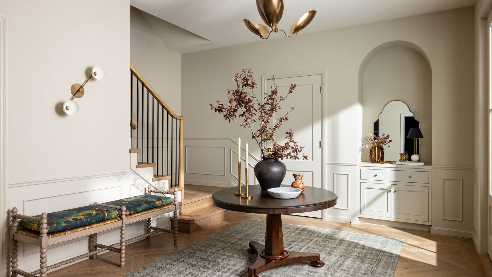 Entry with a round wood table, bobbin bench, herringbone floor and an arched niche with built-in storage.