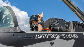 jared isaacman in a jet plane wearing a helmet and pointing up. the words jared rook isaacman are painted on the plane's side