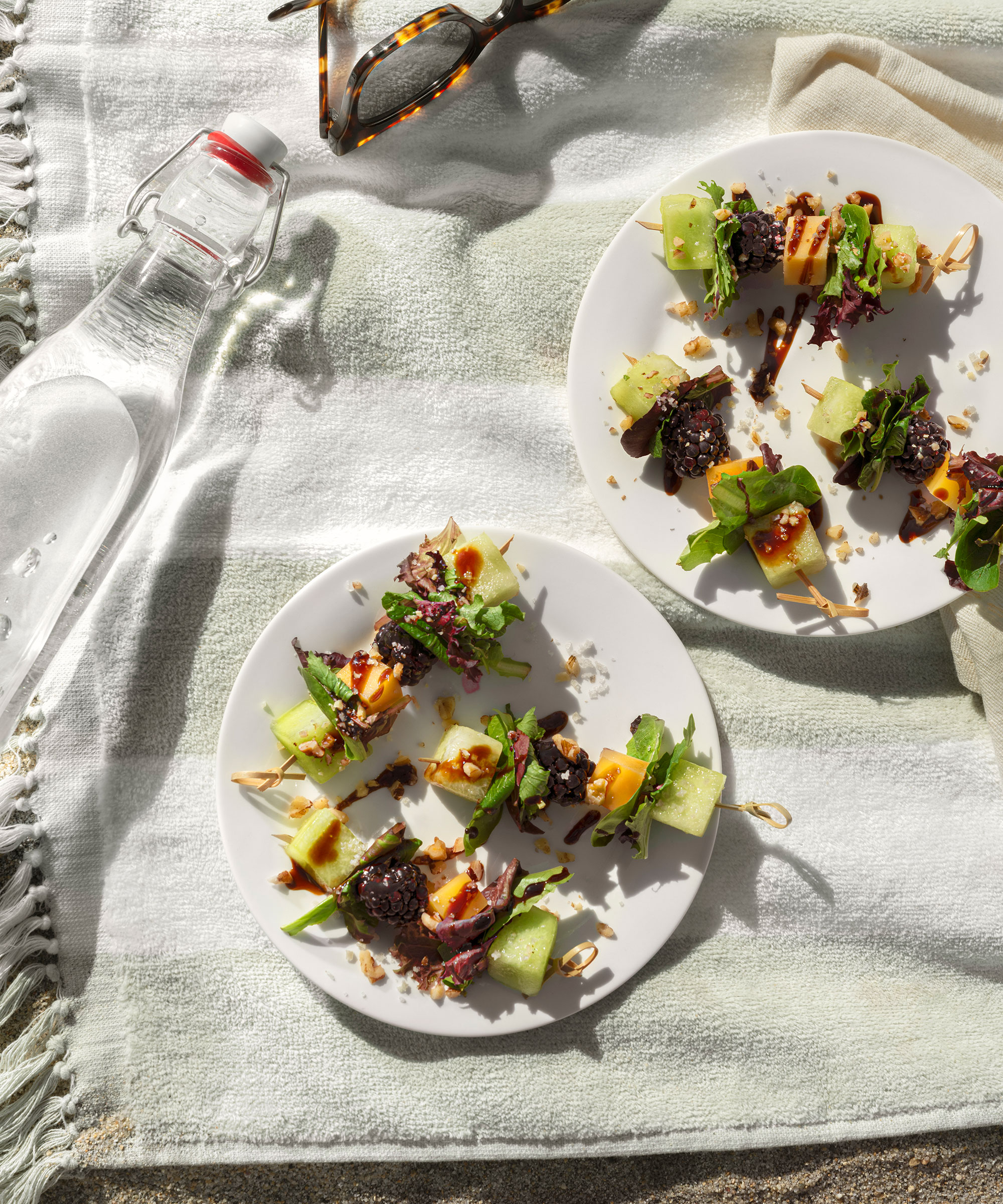 Blackberry Gouda Skewers laid out on a blanket with a bottle of water and sunglasses