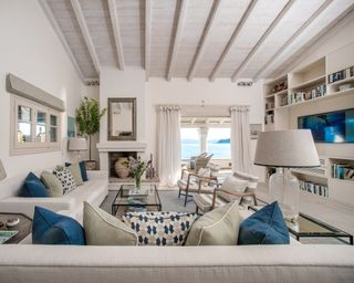 A living toom in a Corfu villa with white vaulted ceilings, blue cushions on white sofas, and a sea view