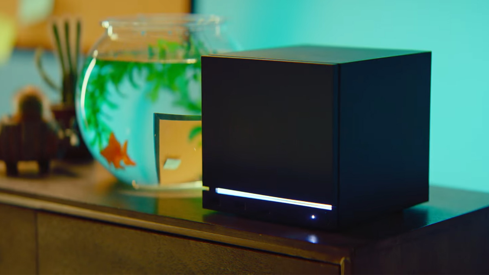 A black cube game console on a wooden shelf