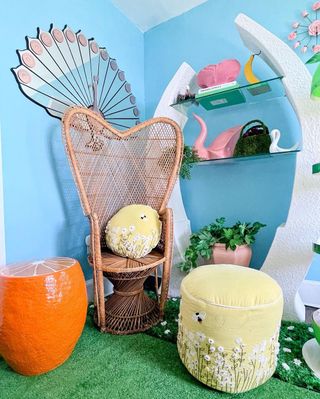 A reading corner with blue walls, a rattan chair, and a yellow footstool