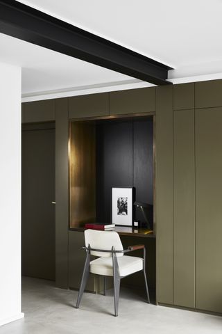 closet office with sage green paneling/doors, gold trimmed desk space, white and metal chair, white walls