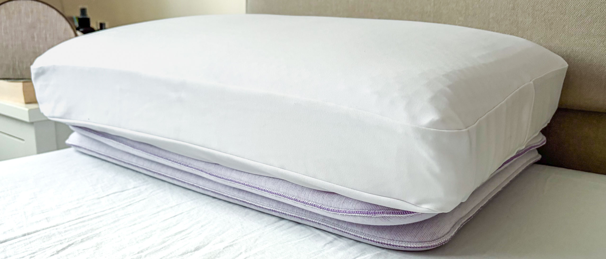 A close up of the Purple DreamLayer Pillow resting on its booster layers, on the bed in our reviewer's bedroom