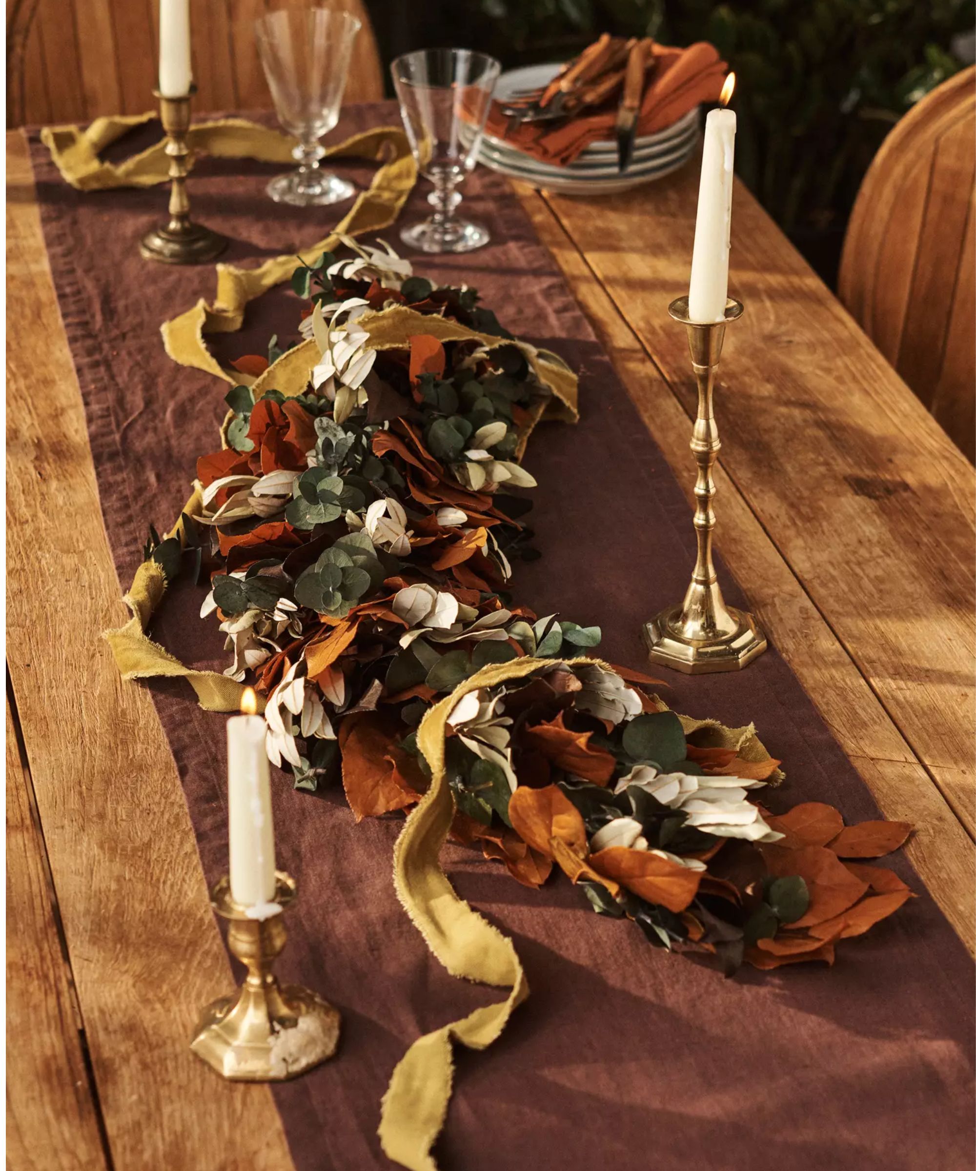Wood dining table with maroon runner, brass candlesticks and a fall leaf centerpiece