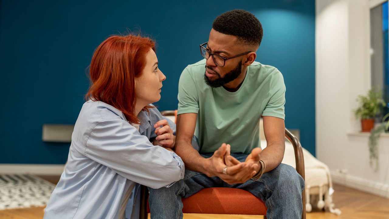 A young couple talk intently in their living room.