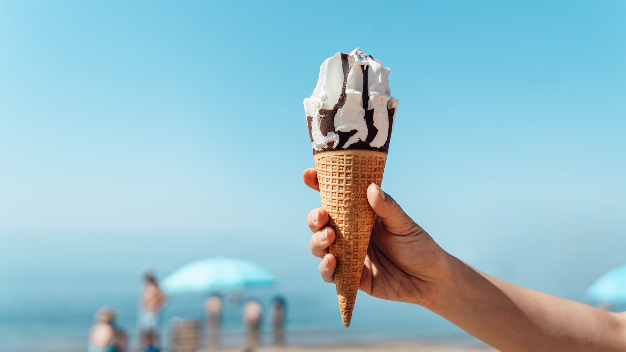Person holding an ice cream cone in front of the sea