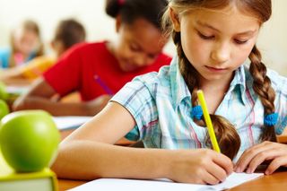 A girl writes in a notebook in a classroom