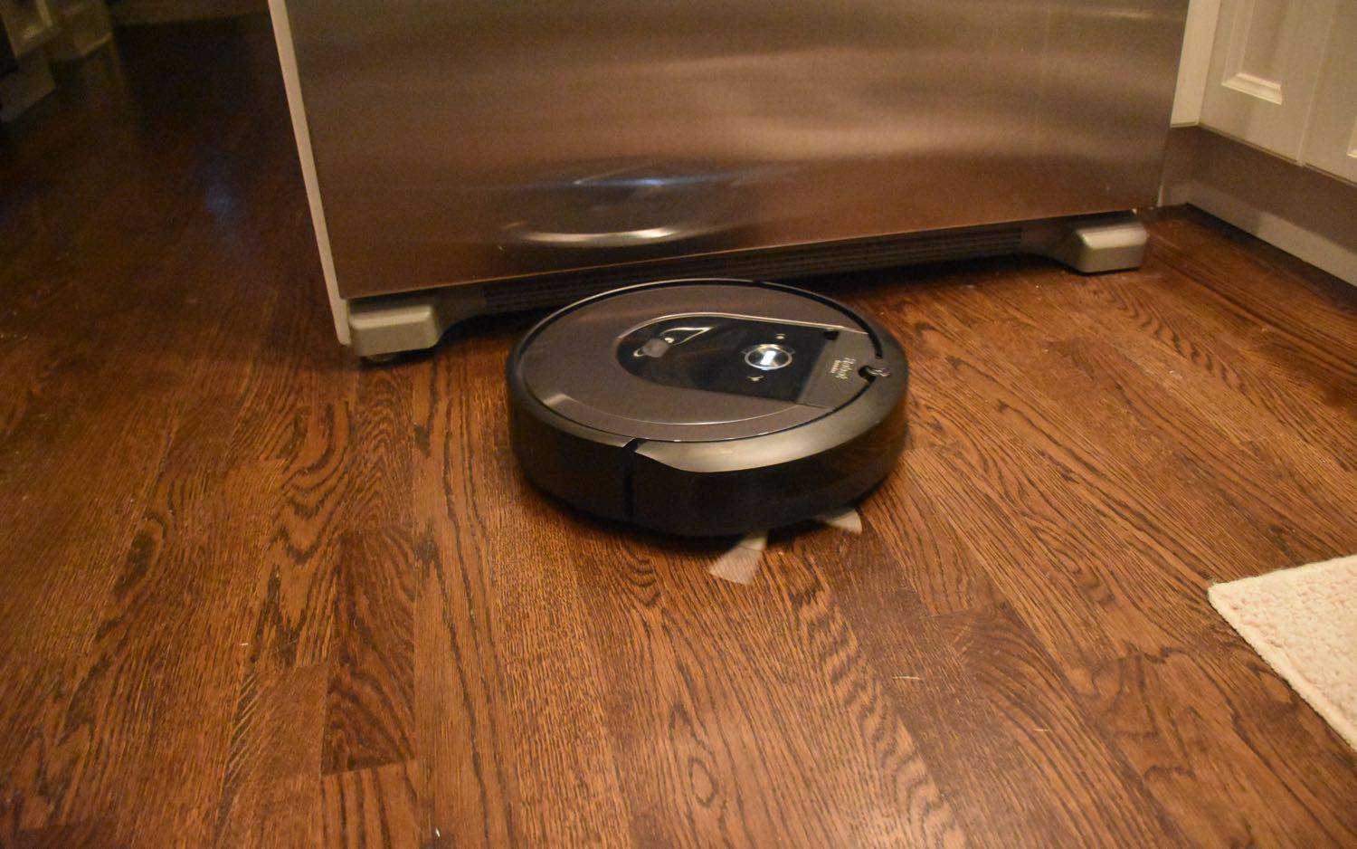 An iRobot Roomba i7+ cleaning dark brown hardwood flooring in kitchen