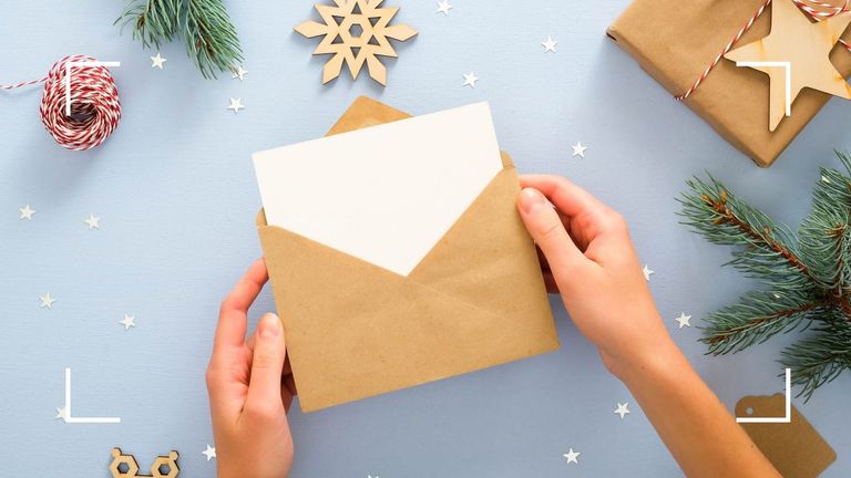 hand placing card in an envelope with christmas decorations scattered around, written with our Christmas card etiquette rules