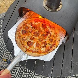 Pepperoni pizza being removed from a pizza oven on a pizza peel