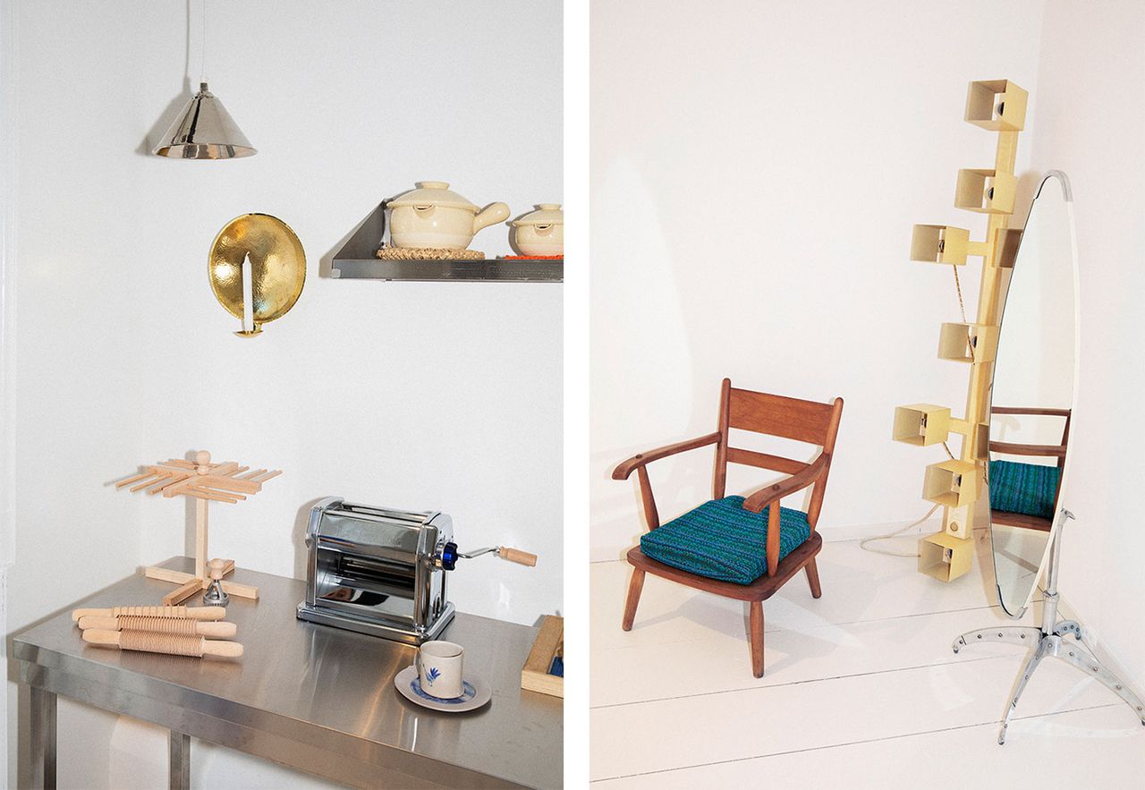 Left, a kitchen top with a pasta maker and wooden fresh pasta drying rack, on the shelves are white ceramic pots and hanging is a silver cone-shaped lamp. Right, a wooden chair with blue upholstery and an oval freestanding mirror