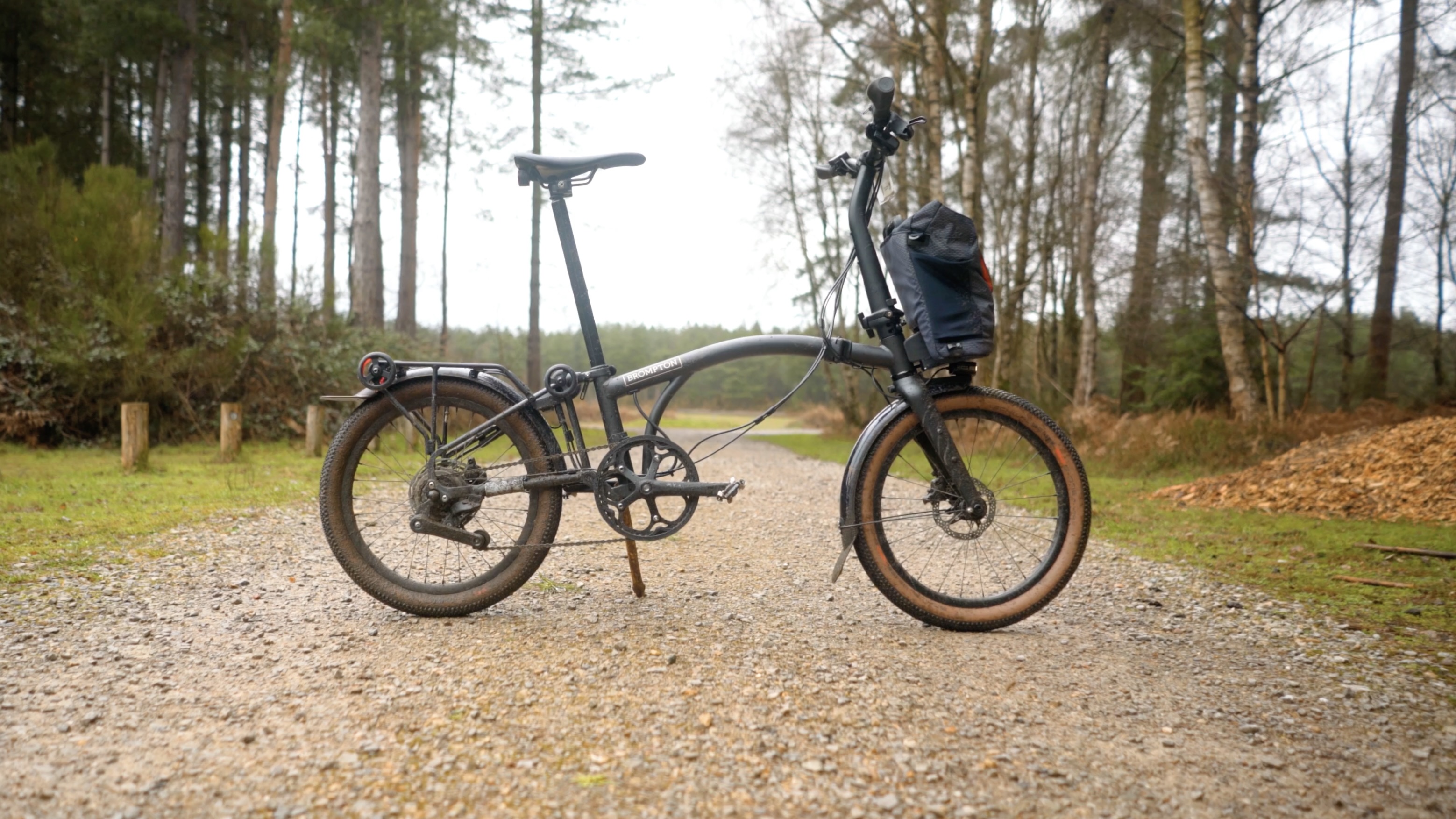 An orange Brompton covered in mud on a light gravel track