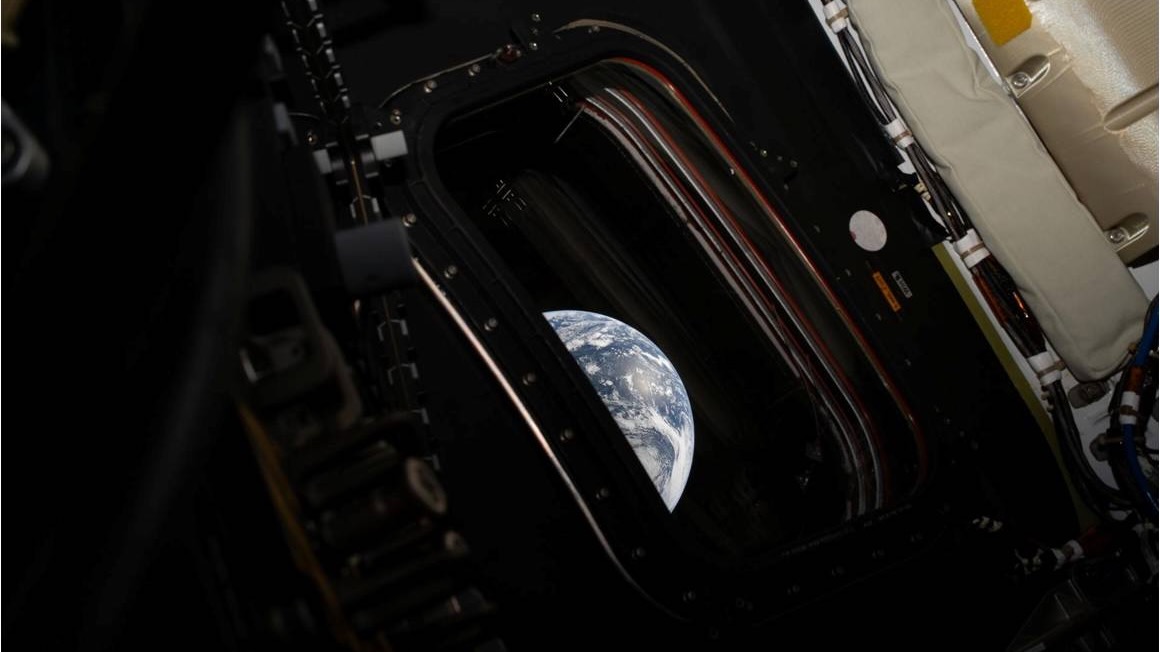 Earth is seen through a small window on a voyaging spacecraft