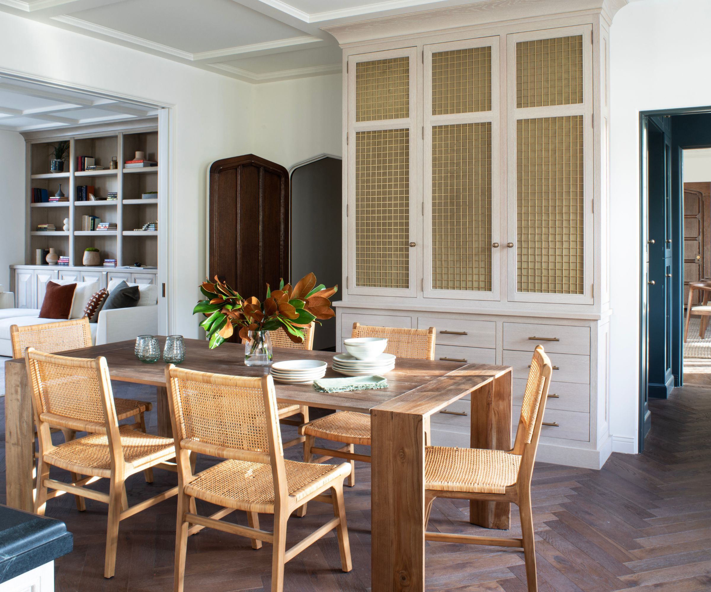 Dining area in an open plan kitchen with white walls and a wooden table with rattan chairs and large beige dresserkitchen