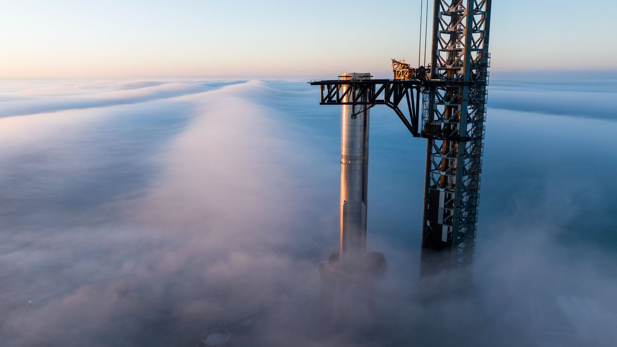 a silver rocket stands on a launch pad with fog swirling around it just after sunrise