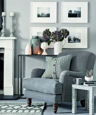 grey living room with a grey sofa chair next to a white fire place and a black table topped with purple flowers and accessories