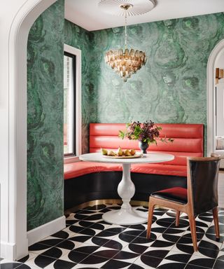 colors that go with red, dining space with red bench seating, black and white tiled floor, white round table, dining chair, chandelier, emerald green marble style wallpaper