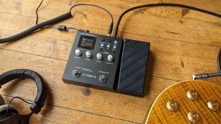 The NUX MG-300 on a wooden floor with an electric guitar and a pair of headphones