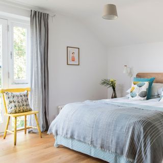 White bedroom with grey curtains, wooden floor and yellow chair