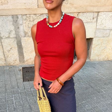 Woman in a red top and navy skirt with a beaded necklace