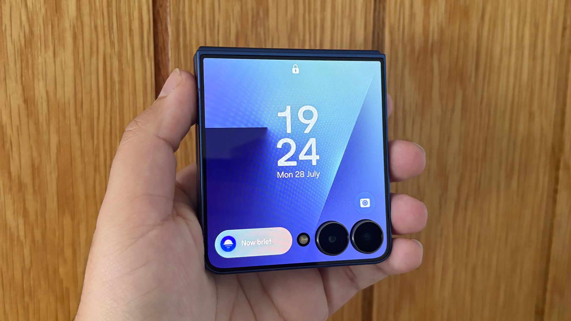 Samsung Galaxy Z Flip 7 smartphone held in hand in folded position against wooden wall