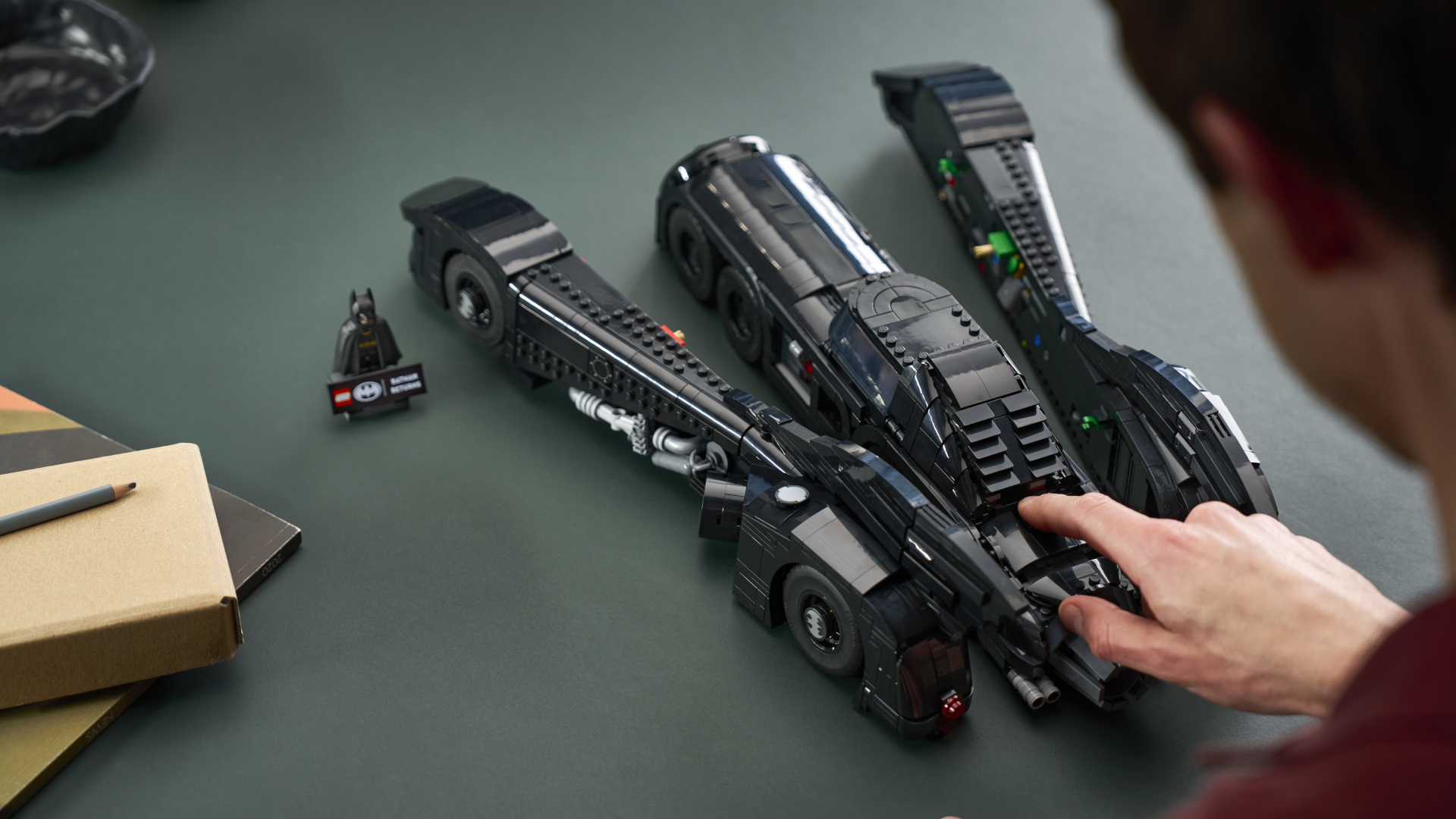 Someone presses a button on the Lego Batman Returns Batmobile to split it apart as it sits on a table beside a minifigure of Batman