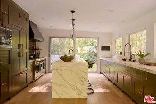 A kitchen with green inset shaker cabinetry, a marble waterfall island, and wooden floorboards