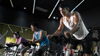 Young people riding stationary bike during indoor cycling class in gym.
