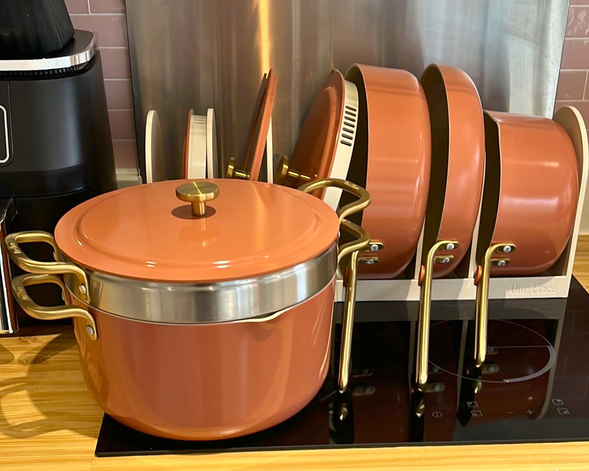 First impressions of the Our Place 11-Piece Essentials Cookware Set, pictured in its organizer rack, on my stove. The strainer is nestled between the stock pot and its lid, and at the front of the stove