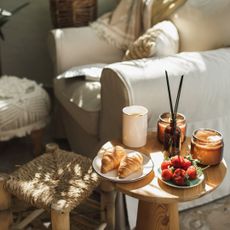 A reed diffuser on a side table with candles and croissants next to an arm chair