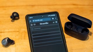 Heardle displayed on a phone with earbuds next to it