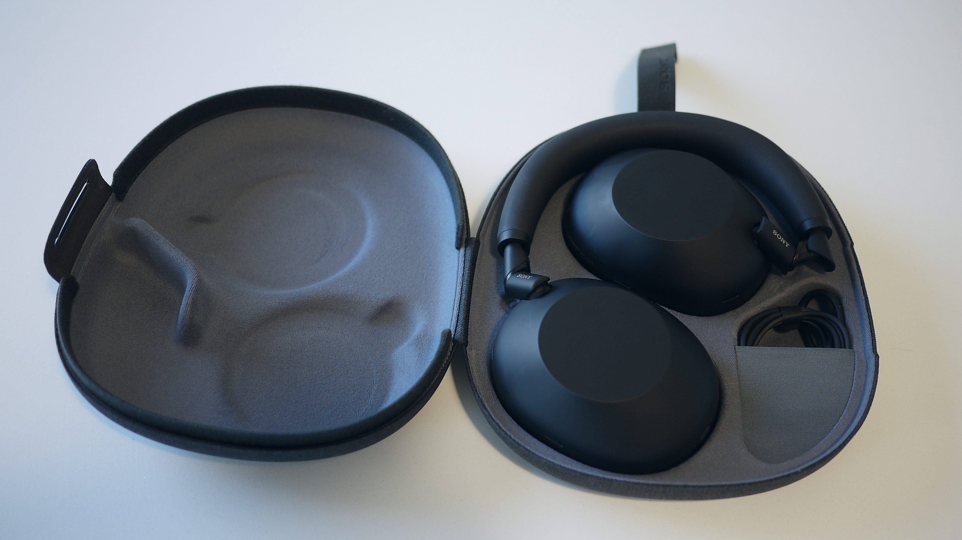 Sony WH-1000XM6 ligger p&amp;aring; et bord i det &amp;aring;bne etui.