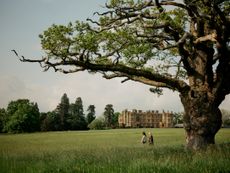 Two women walking in a meadow with a big stone building in the background