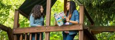 Image of two girls standing in a tree house reading The Week Junior