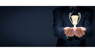 Man in blue suit holds glowing golden trophy cup in his hands