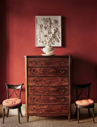 Red painted hallway with antique chest of drawers and two chairs on either side