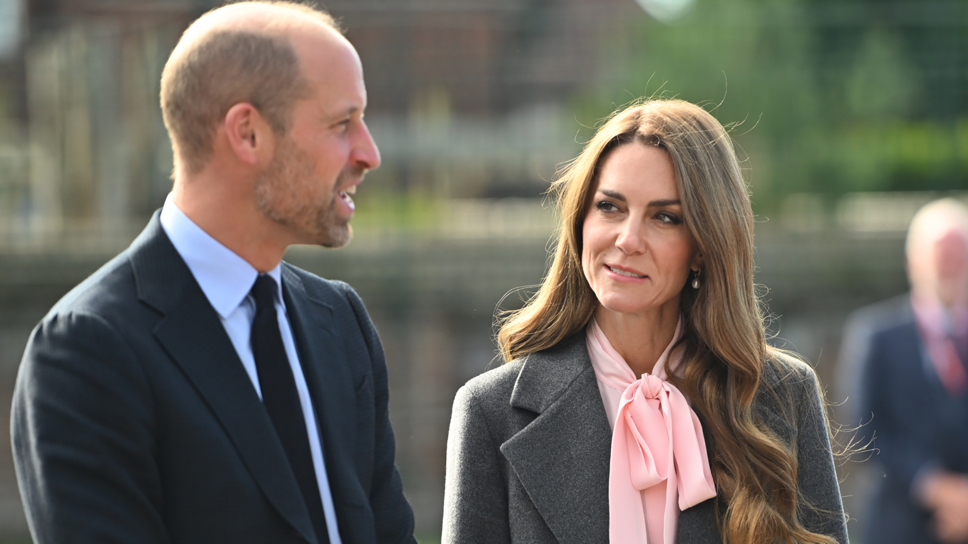 Kate Middleton wearing a gray suit and pink blouse smiling