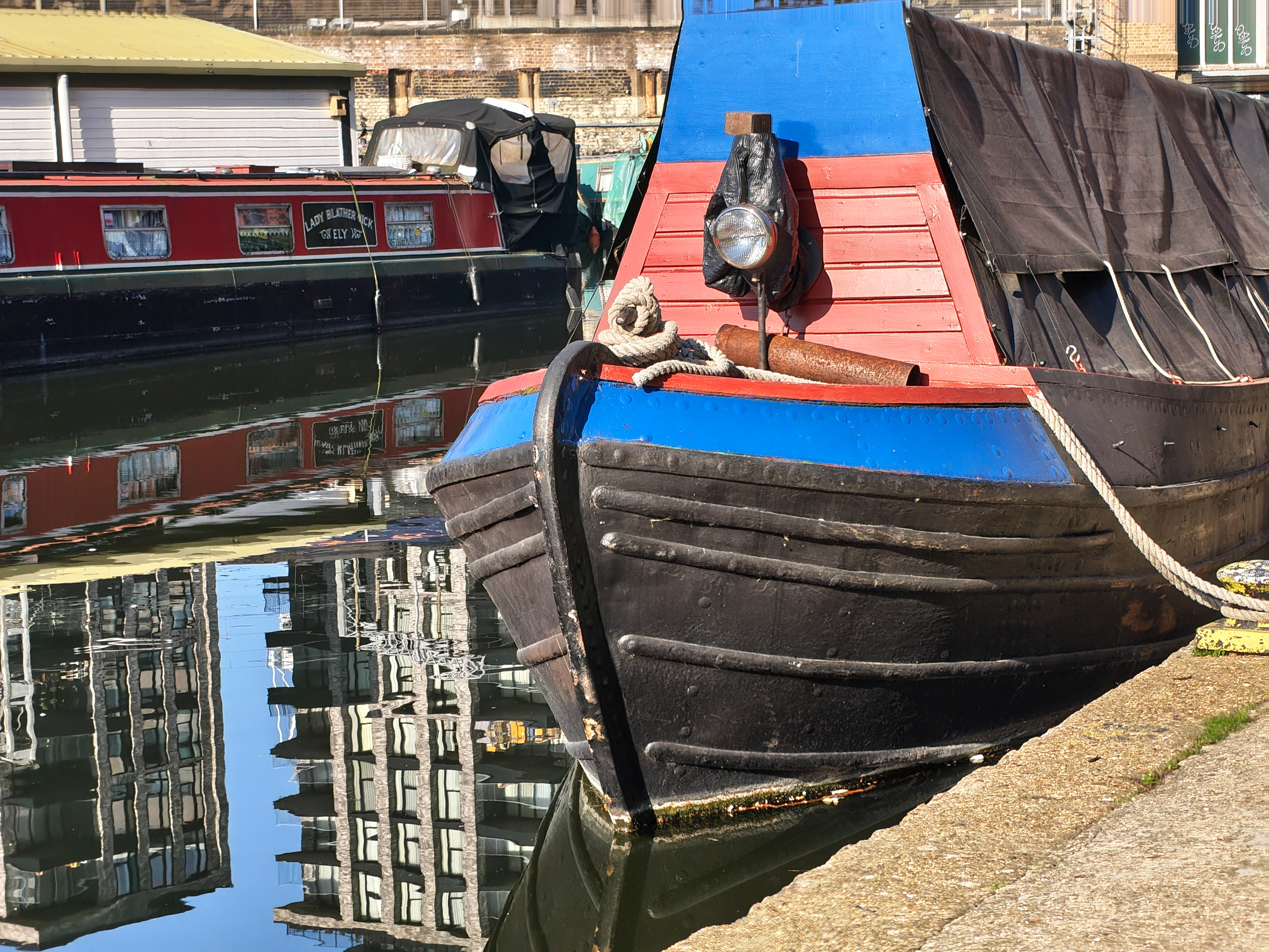 Colorful narrowboats moored along a canal with reflections in the water at St Pancras Yacht Basin, photographed with the Nothing Phone (4a).