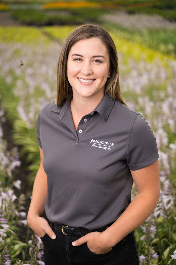 Woman smiling in gray shirt in front of flowers